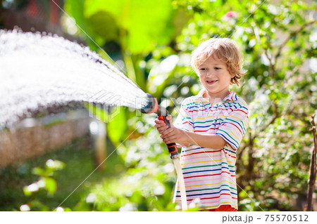 Boy watering flower in garden. Kid with water hose 75570512