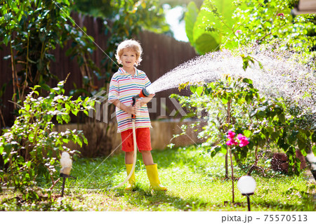 Boy watering flower in garden. Kid with water hose 75570513