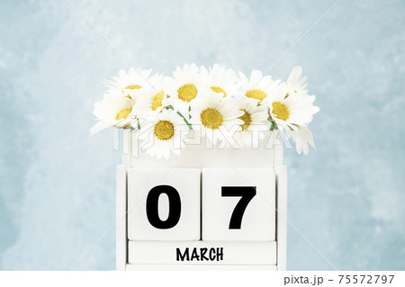 cube calendar for March with daisy flowers over blue with copy space 75572797