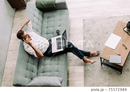 young man is talking on a smartphone, sitting on the sofa. 75572989