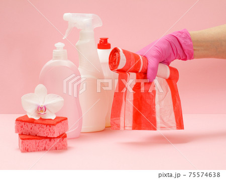 Bottles of dishwashing liquid, sponges and hand with garbage bags on a pink background. 75574638
