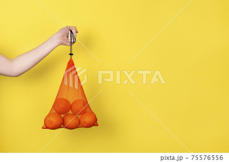 Female hand holding Oranges in eco bag for grocery isolated on yellow. Eco friendly Shopping Bag concept. Banner with copy space. Female hand holding Oranges in eco bag for grocery isolated on yellow. Eco friendly Shopping Bag concept. Banner with copy space. 75576556