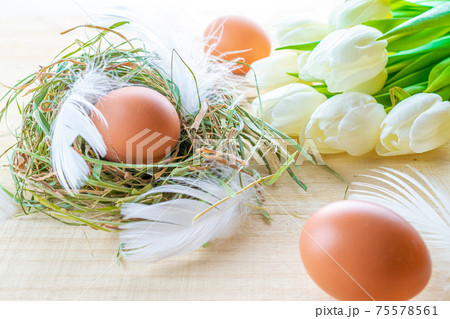 Natural easter colour eggs in basket with spring tulips, white feathers on wooden table background in Happy Easter decoration. Spring holiday concept. 75578561
