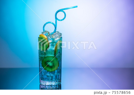 A glass of water with ice and slices of kiwi standing on a mirror table in neon light. Body detoxification or detoxication concept A glass of water with ice and slices of kiwi standing on a mirror table in neon light. Body detoxification or detoxication concept 75578656