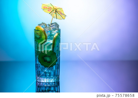 A glass of water with ice and slices of kiwi standing on a mirror table in neon light. Body detoxification or detoxication concept 75578658