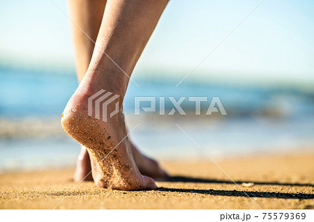 Close up of woman feet walking barefoot on sand leaving footprints on golden beach. Vacation, travel and freedom concept. People relaxing in summer. 75579369