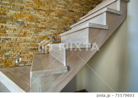 Stylish wooden contemporary staircase inside loft house interior. Modern hallway with decorative limestone brick walls and white oak stairs. Stylish wooden contemporary staircase inside loft house interior. Modern hallway with decorative limestone brick walls and white oak stairs. 75579603