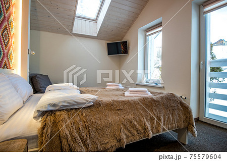 Interior of a spacious hotel bedroom on attic floor with fresh linen on a big double bed. Cozy contemporary mansard room in a modern house. Interior of a spacious hotel bedroom on attic floor with fresh linen on a big double bed. Cozy contemporary mansard room in a modern house. 75579604