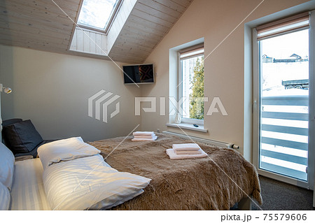 Interior of a spacious hotel bedroom on attic floor with fresh linen on a big double bed. Cozy contemporary mansard room in a modern house. 75579606