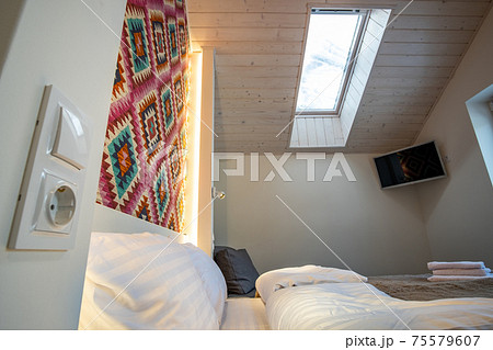 Interior of a spacious hotel bedroom on attic floor with fresh linen on a big double bed. Cozy contemporary mansard room in a modern house. Interior of a spacious hotel bedroom on attic floor with fresh linen on a big double bed. Cozy contemporary mansard room in a modern house. 75579607