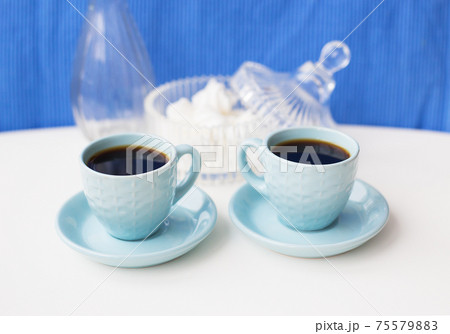 Two blue coffee cup on the table with a vase and saucer with marshmallows 75579883