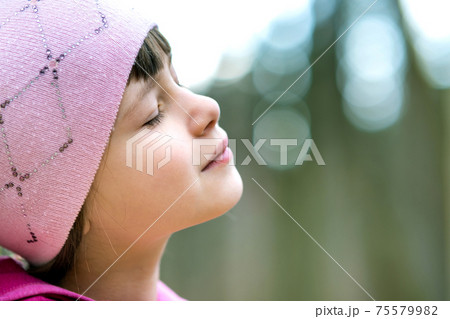 Portrait of young pretty child girl wearing pink jacket and cap enjoying warm sunny day in early spring outdoors. 75579982