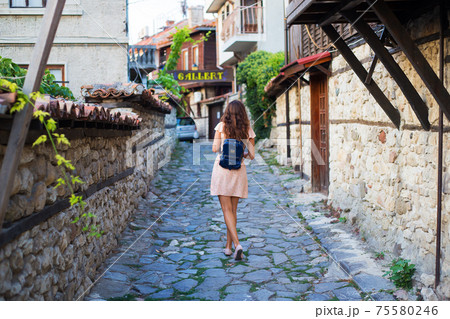 A girl walks through the old streets with a backpack on her back 75580246