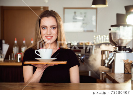 Beautiful female barista is working in coffee shop. Attractive woman is standing behind the bar 75580407