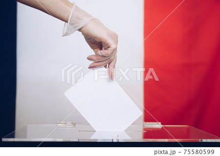 Woman's hand in medical glove throwing her vote into the ballot box. 75580599