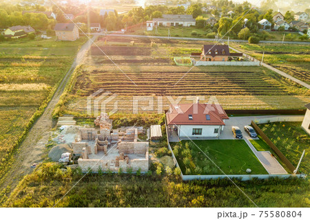 Top down aerial view of two private houses, one under construction with concrete foundament and brick walls and another finished with red tiled roof. Top down aerial view of two private houses, one under construction with concrete foundament and brick walls and another finished with red tiled roof. 75580804