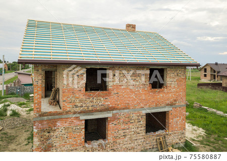 Aerial view of a brick house with wooden roof frame under construction. 75580887