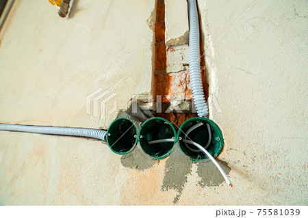 New electrical wiring installation, plastic boxes and electrical cables for future outlet sockets on the wall, renovation concept. New electrical wiring installation, plastic boxes and electrical cables for future outlet sockets on the wall, renovation concept. 75581039