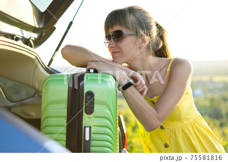 Young female driver having rest leaning on a green suitcase near her car in summer nature. Travel and vacations concept. 75581816