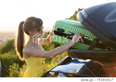 Young woman taking green suitcase out from car roof rack. Travel and vacations concept. 75581817