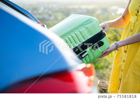 Close up of female hands taking green suitcase from car trunk. Travel and vacations concept. 75581818