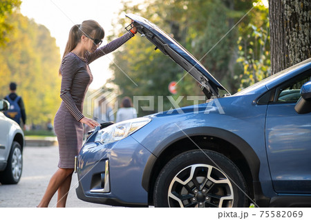 Young woman driver standing near a broken car with open hood having trouble with her vehicle Young woman driver standing near a broken car with open hood having trouble with her vehicle 75582069