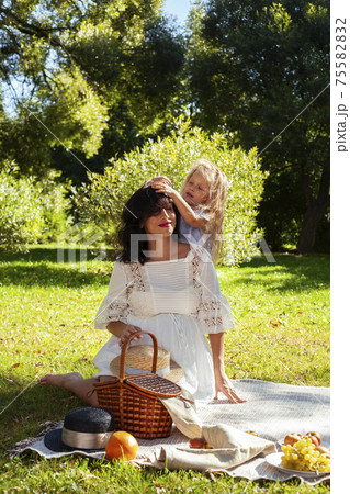 young pretty pregnant brunette woman having fun with her daughter on picnic on green grass in park, lifestyle people concept 75582832