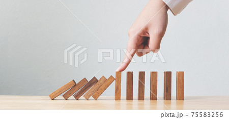 Hand stopping wooden domino business crisis effect or risk protection concept 75583256