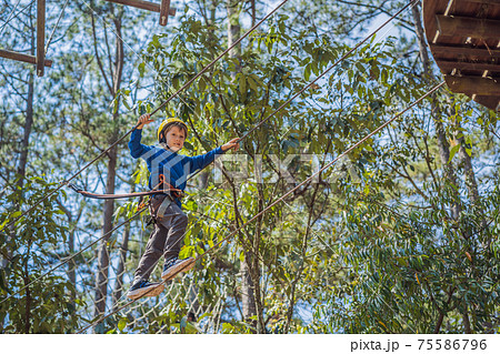 Happy child in a helmet, healthy teenager school boy enjoying activity in a climbing adventure park on a summer day 75586796