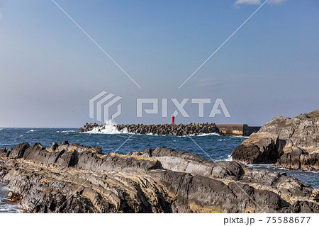 岩場にある港の防波堤の赤色灯台、強風で波が砕ける 75588677