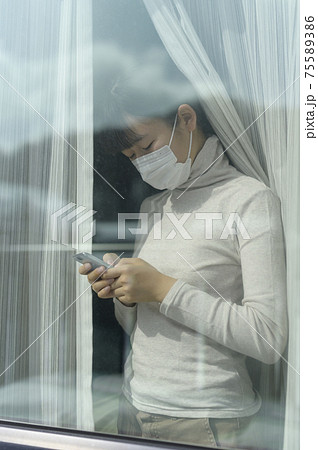 窓辺でスマートフォンを見る女の子（外出自粛要請のイメージ） 75589386