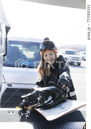 車のトランクからスノーボードを出す若い女性　ウィンタースポーツ 75589391