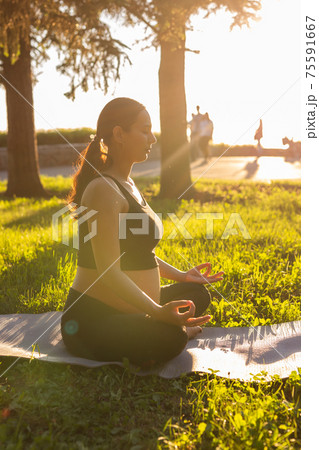 Cute young caucasian pregnant woman is meditating while sitting on a rug on the lawn on a sunny summer evening. Concept of pacification and energy boost 75591667