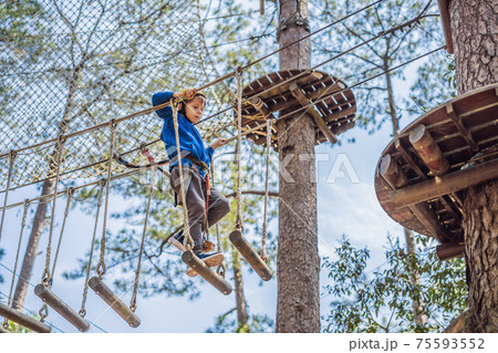Happy child in a helmet, healthy teenager school boy enjoying activity in a climbing adventure park on a summer day 75593552