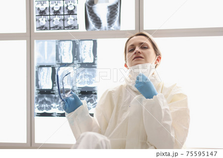 Tired doctor in protective suit sits on floor with X-rays hanging in background 75595147