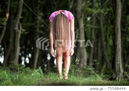 Creepy woman with long hair standing bent down in moody dark forest. Creepy woman with long hair standing bent down in moody dark forest. 75598444