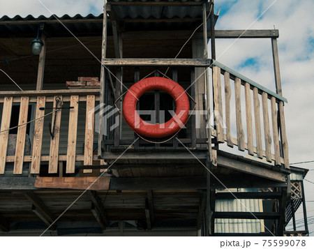 Old retro red lifebuoy hanging on wooden balcony. Help, rescue concept. Vintage life saver on the beach house 75599078