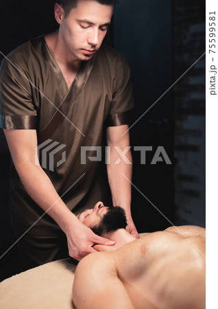 Professional neck massage to a bearded male athlete in a dark room of a spa massage room 75599581
