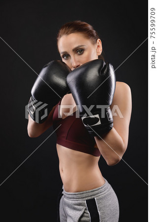 Caucasian fitness girl in boxing gloves stands in a rack on a black background, portrait of a strong and independent woman fighter 75599709