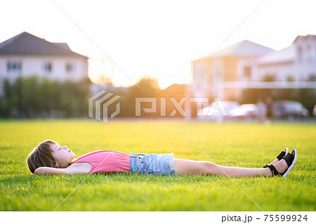 Young pretty child girl relaxing lying down on green grass on warm summer evening. 75599924