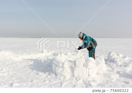 Happy woman building an igloo on the snow Happy woman building an igloo on the snow 75600322