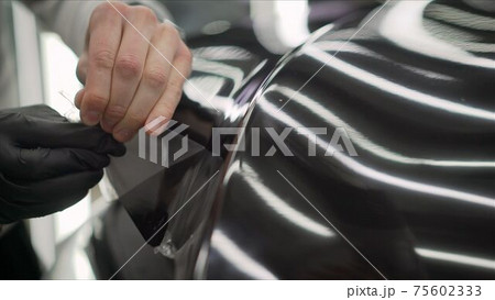 Workers remove the protective film from the machine.Deteyling car. Sticker protective film on the bumper of the car. 75602333