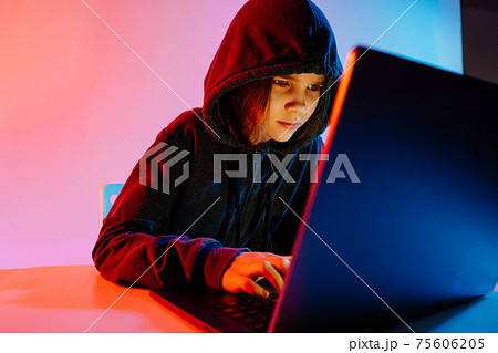 a girl in dark hooded clothes works at night at the computer. Hacker.  75606205