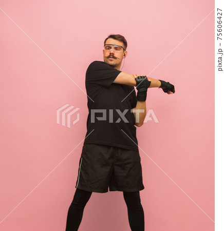 Young athletic man in black sports attire isolated on pink background. 75606427