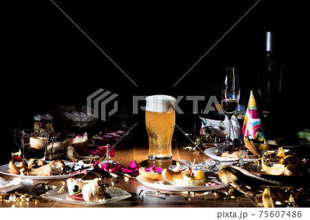 Early morning after the party. Glass of light, cold lager, beer on the table with confetti and serpentine, leftovers, flower petals 75607486