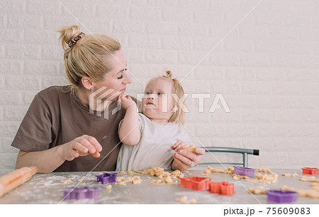 happy young mother and her little daughter together prepare delicious cookies sitting at the table in the home kitchen 75609083