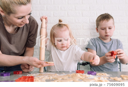 little girl and boy help mom in the kitchen to cook delicious cookies 75609095