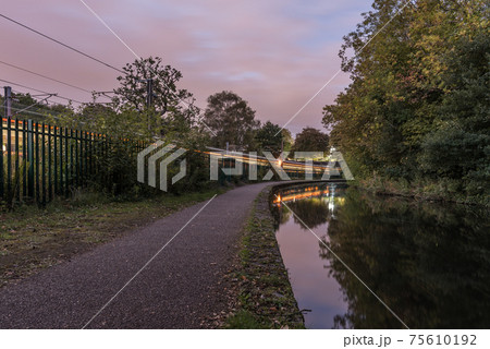Worcester to Birmingham canal, in England, UK. The footpath by the side of the canal, with a train going past along side. The sky is beginning to darken as the sun goes down	 75610192