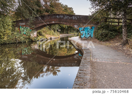 A bridge over the Worcester to Birmingham canal, in England, UK. The bridge is reflected in the very calm waters of the canal. 75610468