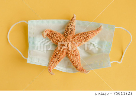 Star fish and face medical mask on yellow background. Coronavirus travel concept. Minimal 75611323